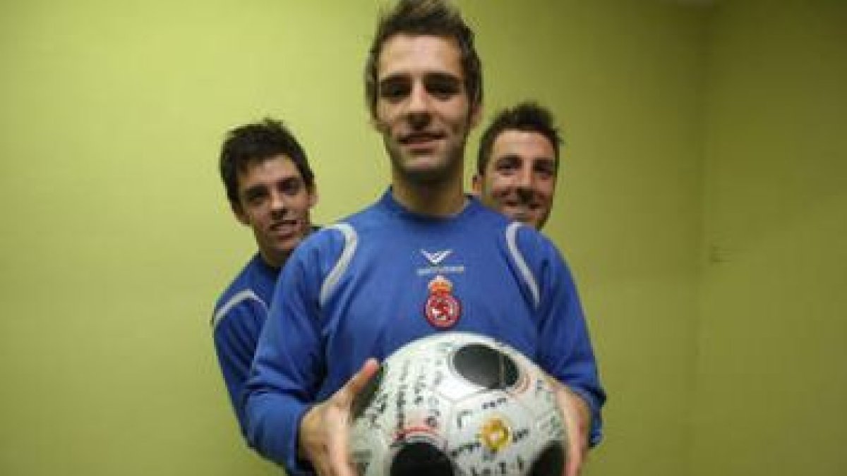 Paixao sostiene un balón firmado por todo el equipo junto a sus compañeros Óscar Rico y Pablo García