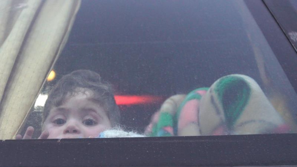 n niño mira por la ventana de un autobús la llegada de civiles y combatientes a la localidad de Qalaat al-Madiq, al sudeste de la ciudad tomada por los rebeldes de Idlib (Siria).