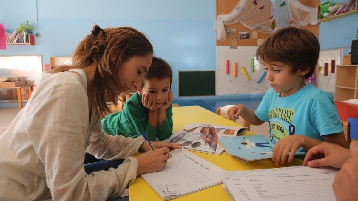 Una maestra conversa con dos niños en el aula de un colegio.