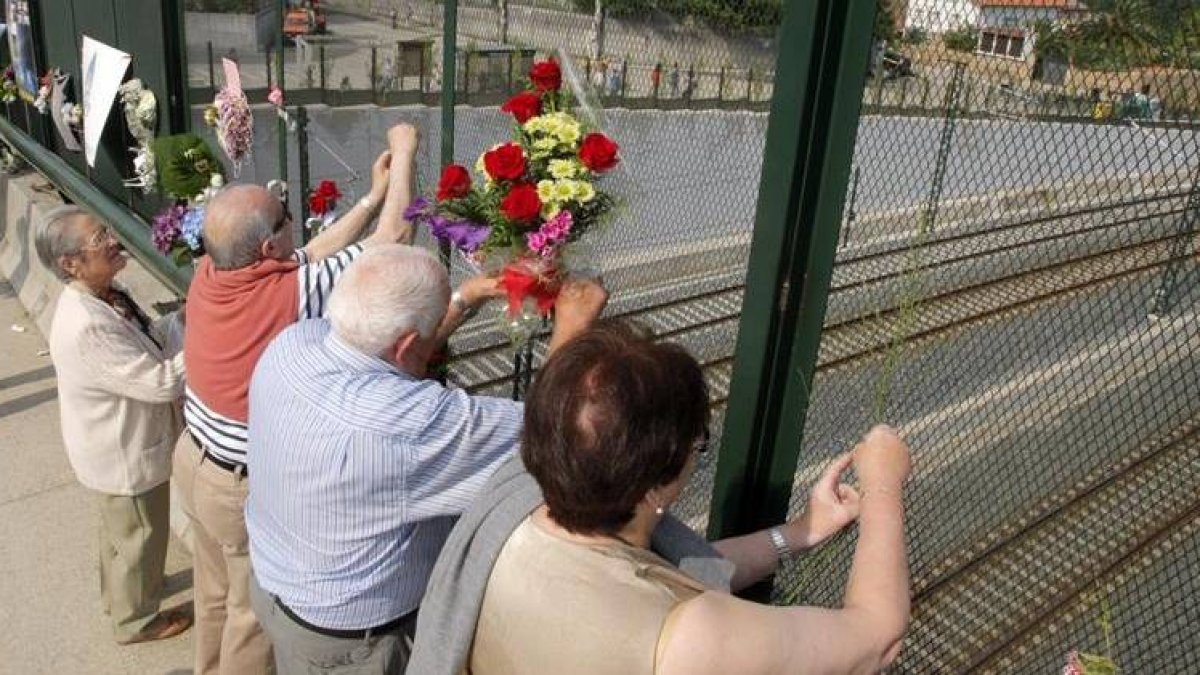 Varias personas colocan flores en el paso sobre la vía del tren.