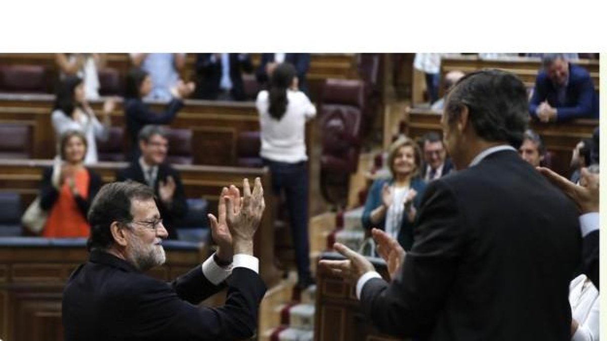 Mariano Rajoy, junto al portavoz parlamentario del PP, Rafael Hernando, aplaude con la bancada popular tras la votación en el pleno del Congreso. Al fondo, de espaldas, Pablo Iglesias recibe la ovación de Podemos y aplaude a su grupo parlamentario.