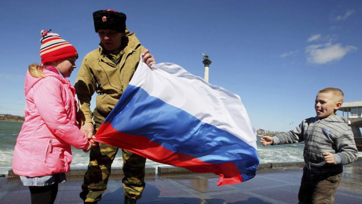 Un hombre sostiene una bandera de Rusia junto a dos niños frente al mar en Sebastopol.
