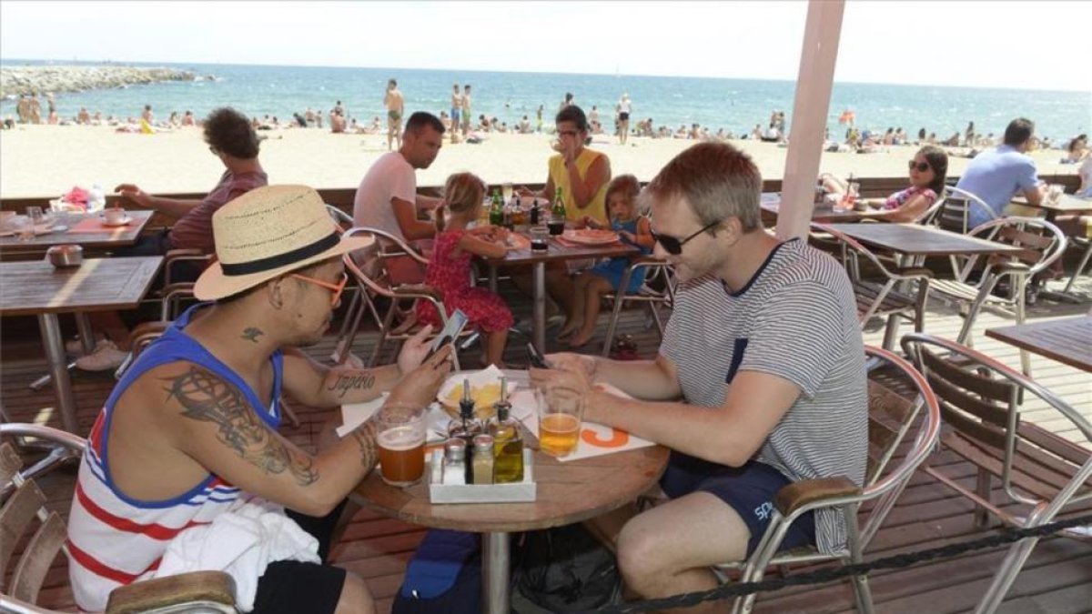 Dos turistas utilizan el móvil en una playa de Barcelona.