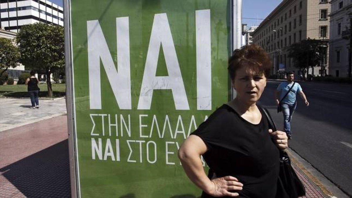 Una mujer espera el autobús junto a un cartel que pide el voto positivo en el referéndum, en el que se lee: "Sí a Grecia, sí al euro".