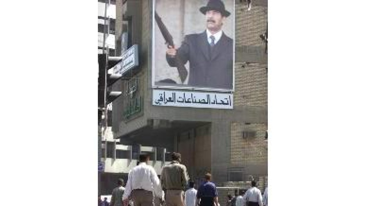 Ciudadanos iraquíes caminan cerca de un cartel de Husein, en Bagdad