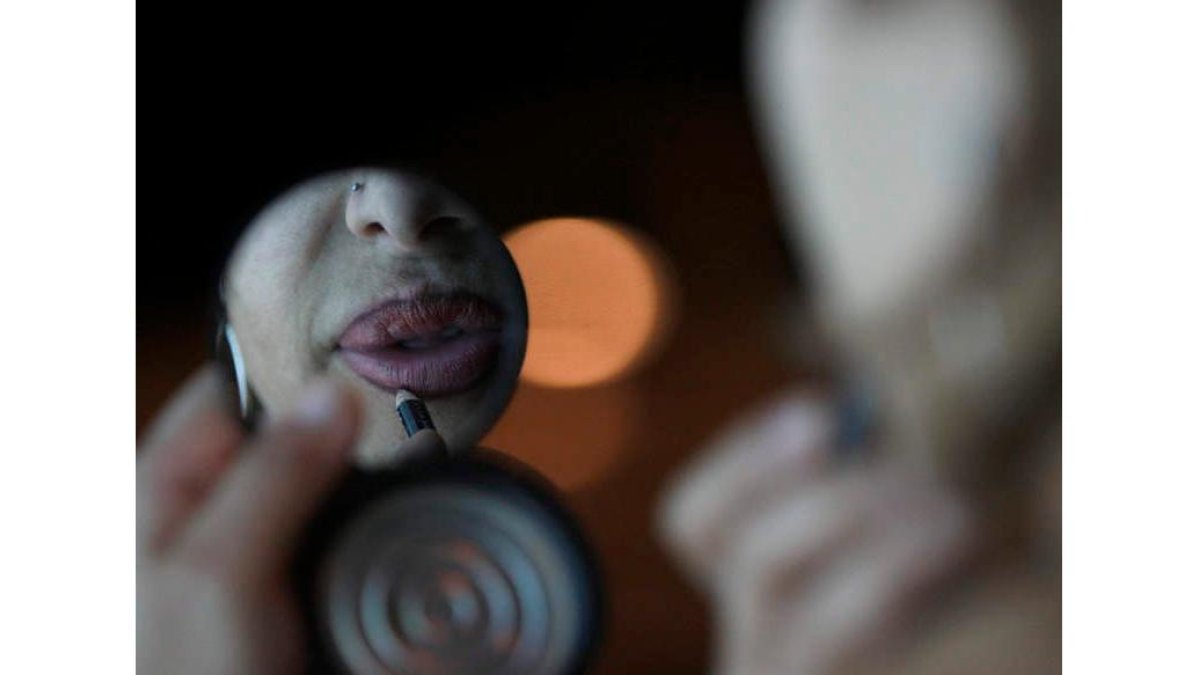 Una mujer que ejerce la prostitución retoca sus labios ante un espejo de mano.