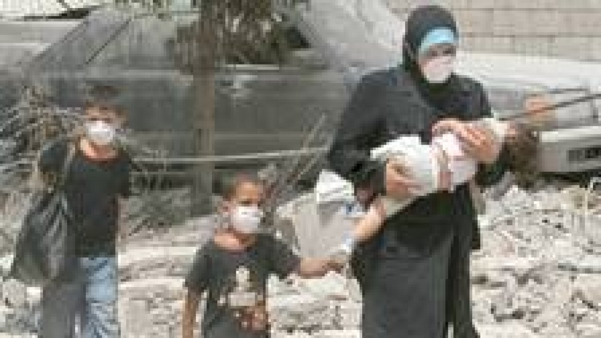 Una mujer libanesa pasa, con sus hijos tapados con máscaras, por delante de los escombros en Beirut