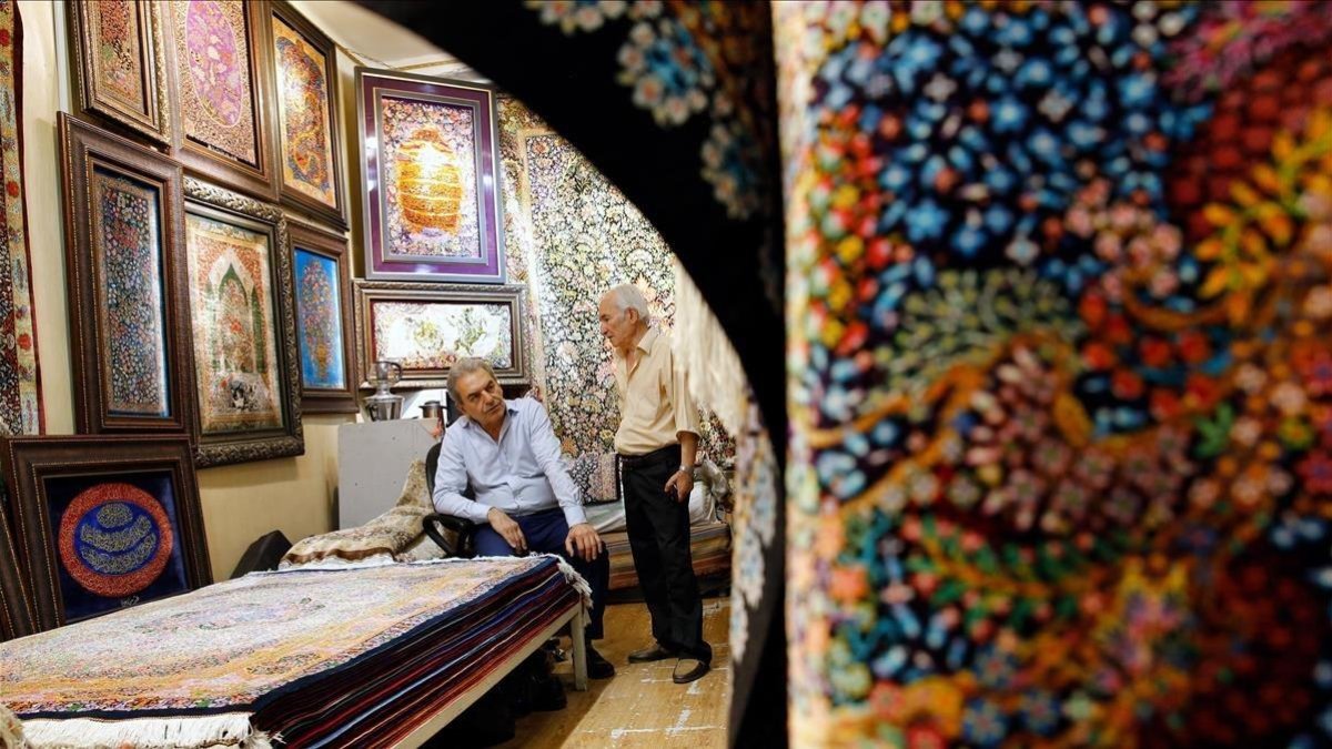 Dos hombres iranís conversan dentro de su negocio de alfombras en el Gran Bazar de Teherán. /