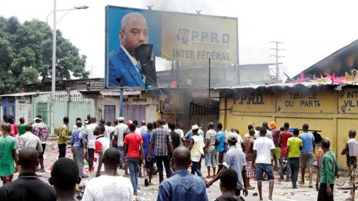 Opositores del presidente Kabila gritan consignas contra el mandatario mientras destruyen un cartel con su imagen, en Kinshasa, capital de la República Democrática del Congo, este lunes.