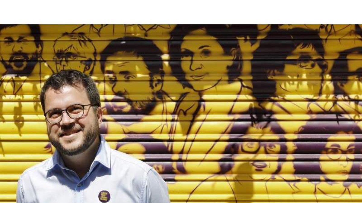 Pere Aragonés ante una trapa pintada con los rostros de los políticos presos en el barrio de Gracia, en Barcelona. ANDREU DALMAU