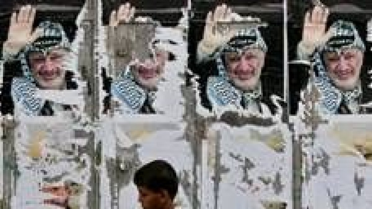 Un niño pasa delante de un muro empapelado con fotos de Arafat, ayer, en Gaza