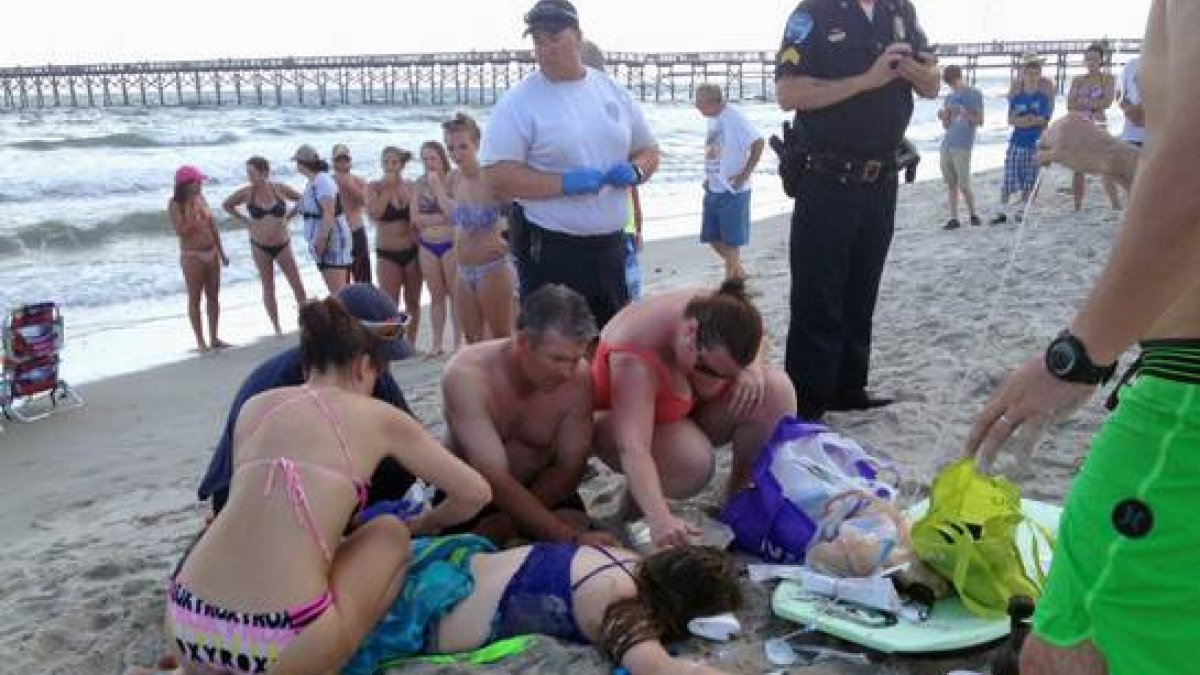 Los servicios de emergencia atienden a la joven de 14 años que ha sido atacada por un tiburón, este domingo en la playa de Oak Island.