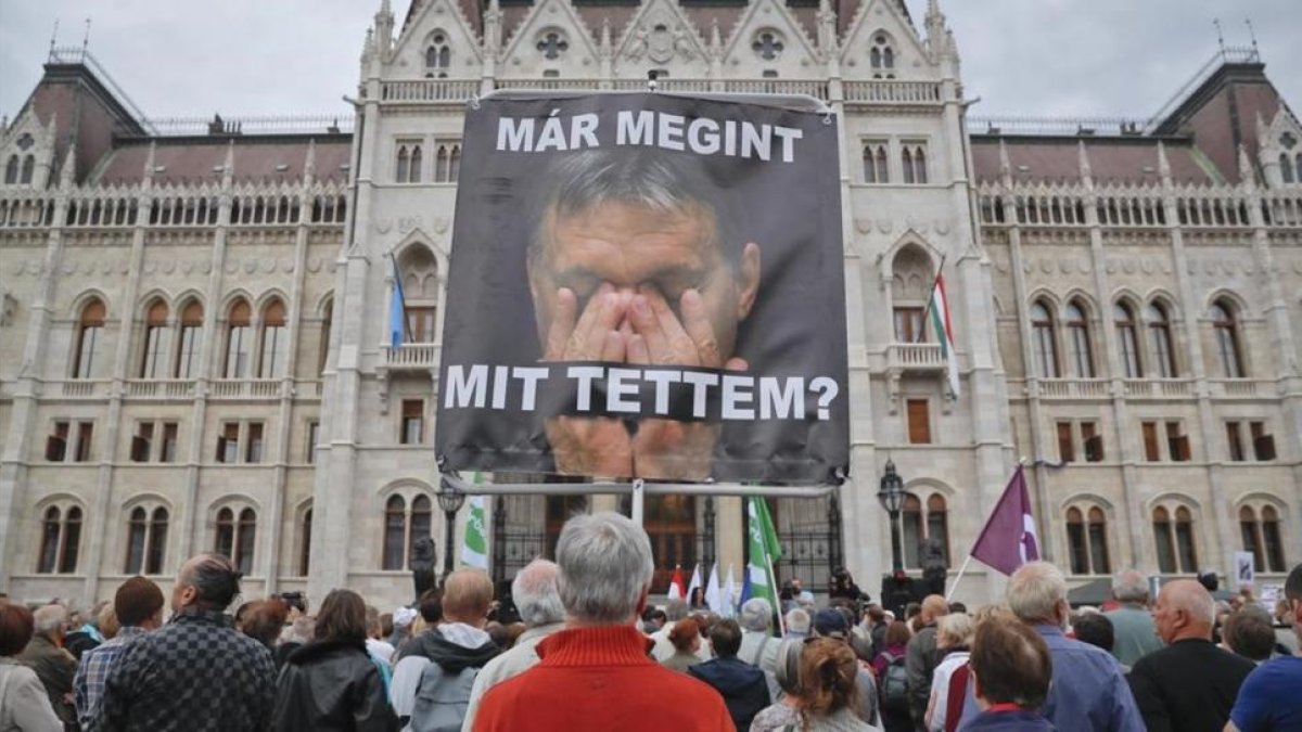Un hombre sostiene un póster con la imagen de Orbán donde se lee: '¿Qué he hecho otra vez?', en un acto de protesta de partidos opositores al presidente húngaro, en Budapest, este domingo.