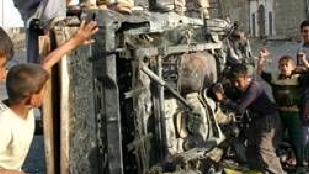 Niños iraquíes buscan gasolina en un coche que ha sufrido un atentado en Bagdad