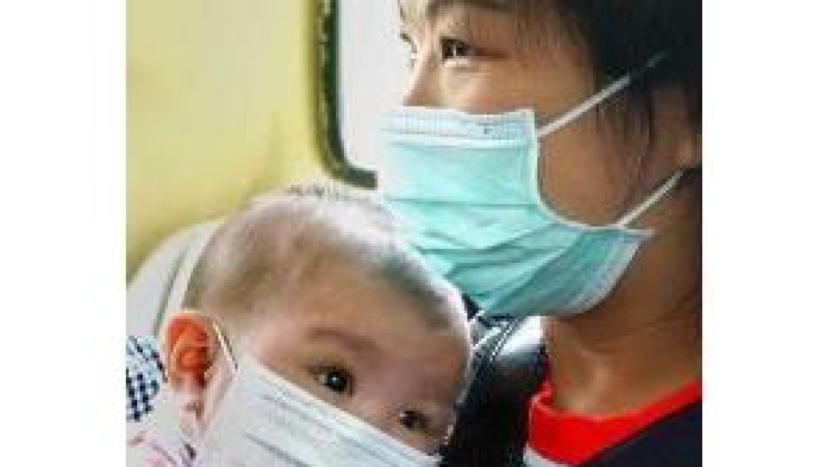 Una madre protege a su bebé con una mascarilla del virus de la neumonía, en un tren de Hong Kong