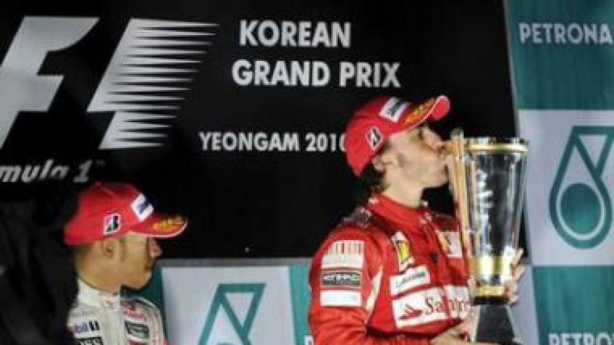 Alonso besa el trofeo ante la mirada de Hamilton.