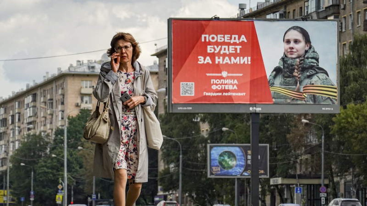 Una mujer rusa pasa ante un cartel que anuncia la mili con el lema «¡La victoria será nuestra!». YURI KOCHETKOV