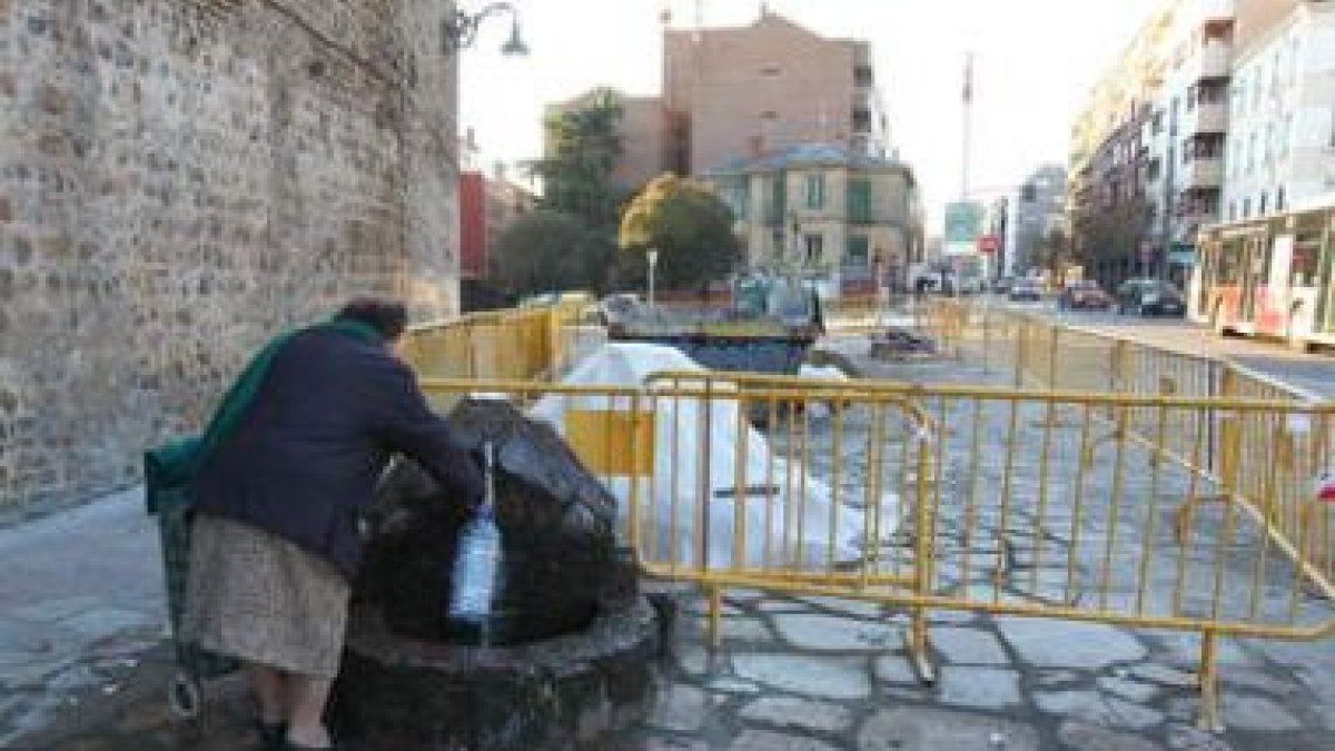 Una mujer coge agua del caño actual; detrás, tapada, la nueva fuente de la plaza.