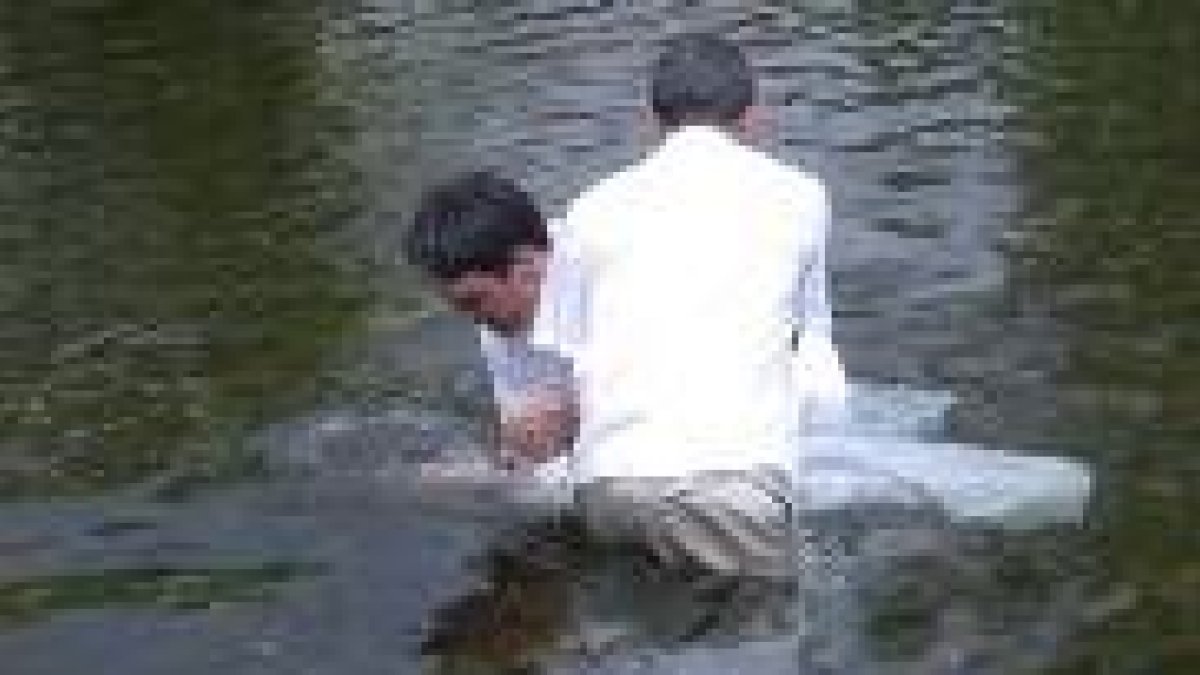 Dos miembros de la comunidad evangélica sumergían a los fieles en las frías aguas del río Luna