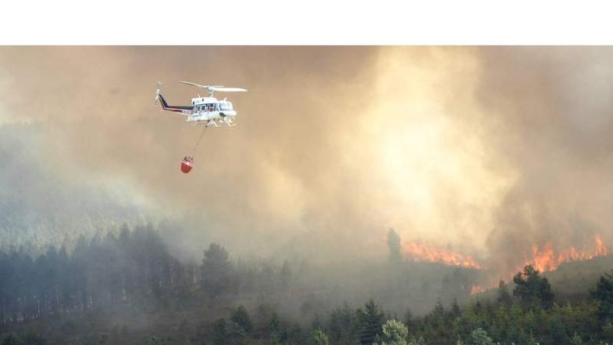 Uno de los helicópteros que participaron en la extinción del fuego se aproxima a las llamas para descargar el agua.