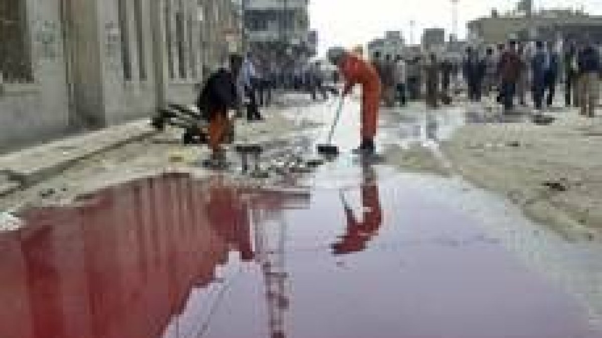 Dos limpiadores arrastran la sangre del atentado de ayer en Hilla