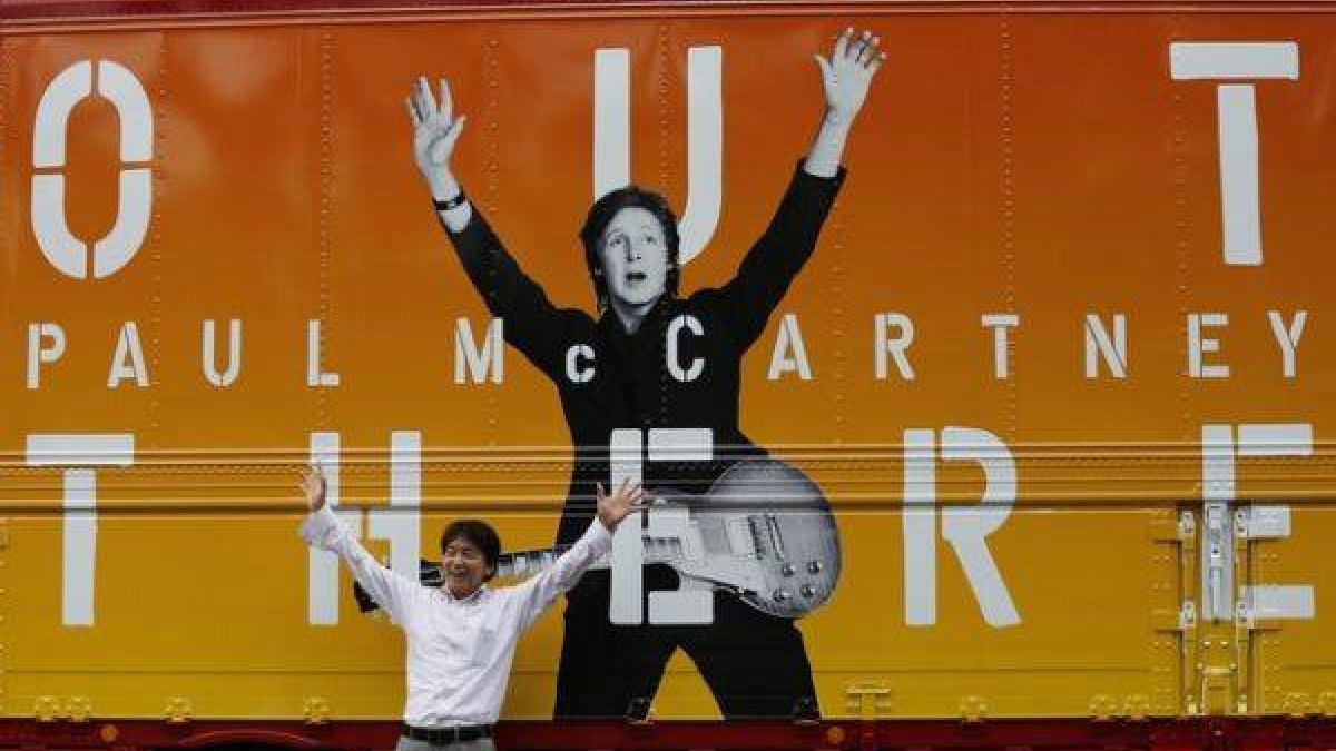 Un hombre posa junto a un cartel de la gira de Paul McCarney en Japón que, finalmente, se ha cancelado.