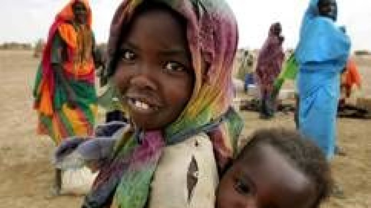 Una niña sonríe al fotógrafo con su hermano a la espalda en un campo de refugiados en Darfur