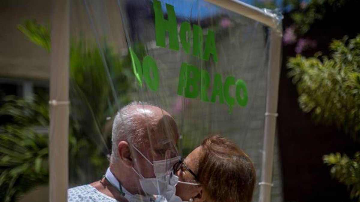 La pareja que celebrará en una semana 50 años de matrimonio, Walter Candido (paciente), de 75 años, y Marlene Amaral (visita), de 73, se besan entre una lámina plástica usada para que pacientes y familiares puedan abrazarse. ANTONIO LACERDA