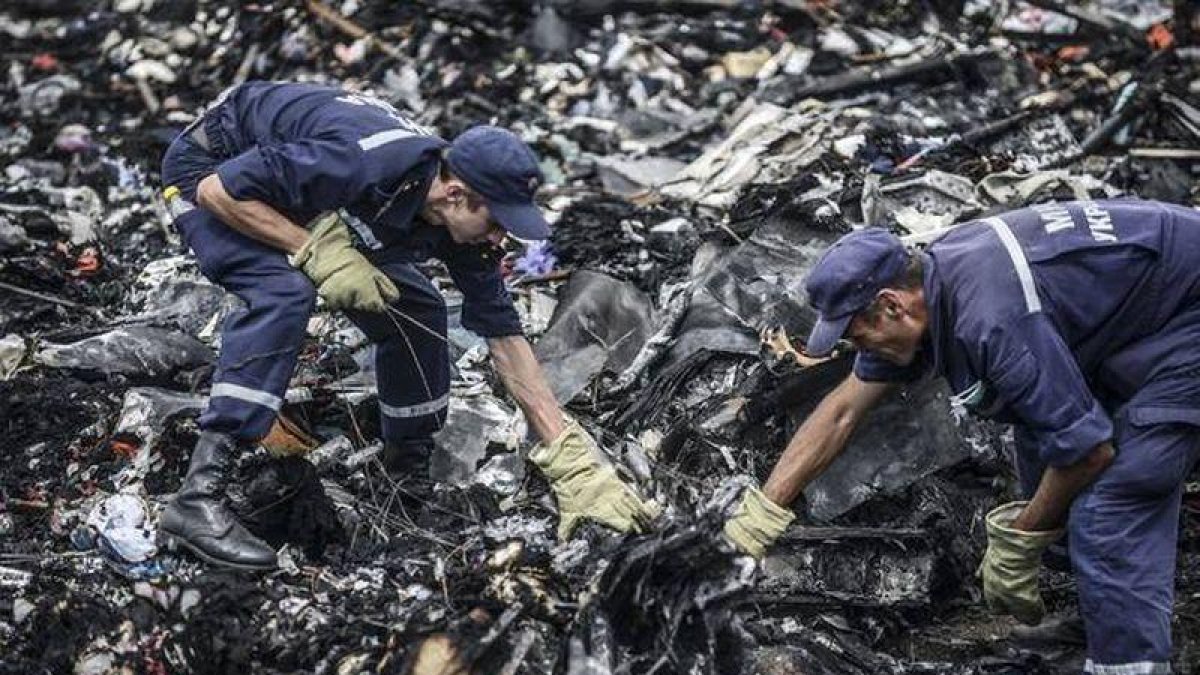 Dos agentes buscan entre los restos del vuelo MH17 de Malaysia Airlines.