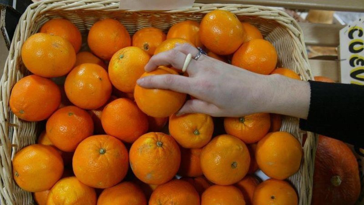 Una persona coge una naranja en un supermercado.
