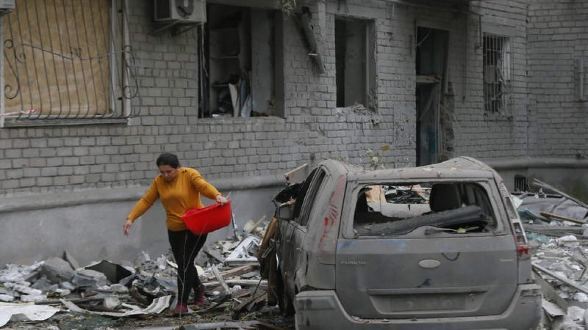 Una mujer lleva algunas pertenencias entre los escombros de su casa, alcanzada por un bombardeo. STR