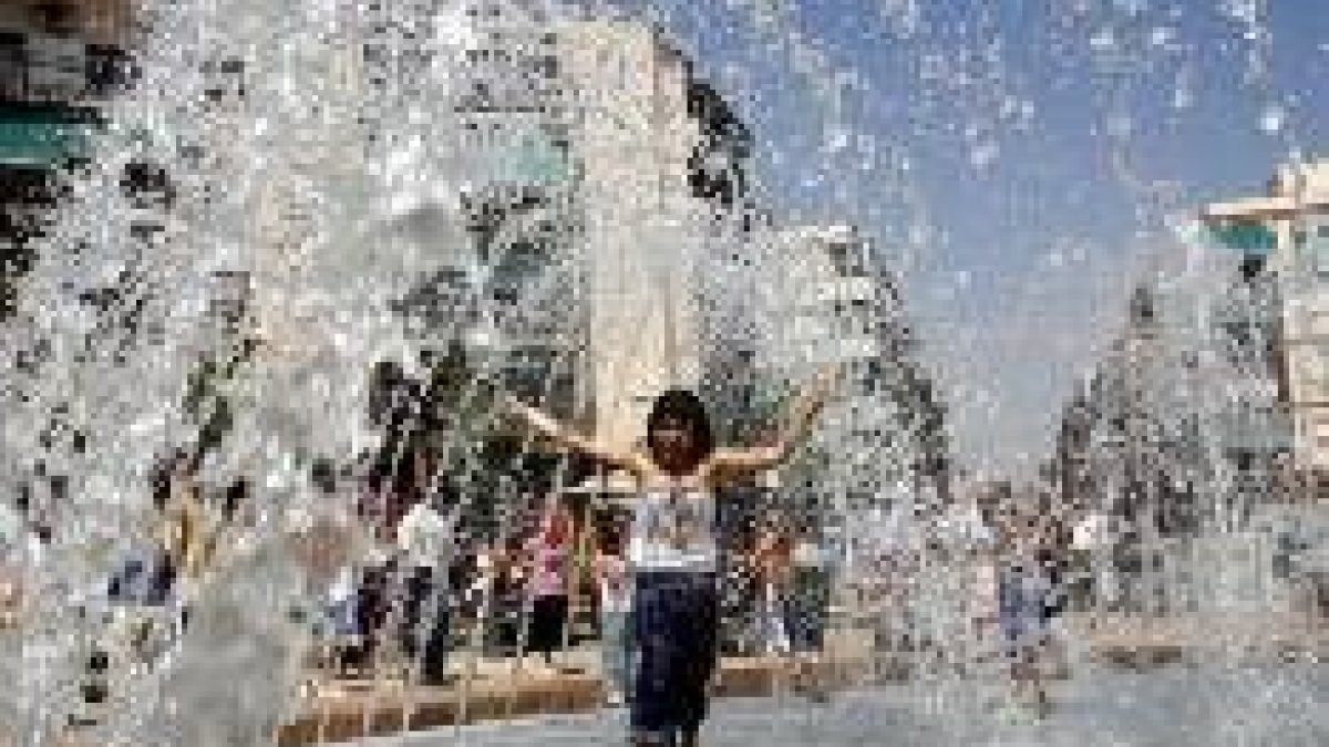Una niña combate el calor al pasar bajo los surtidores de una fuente en Alicante