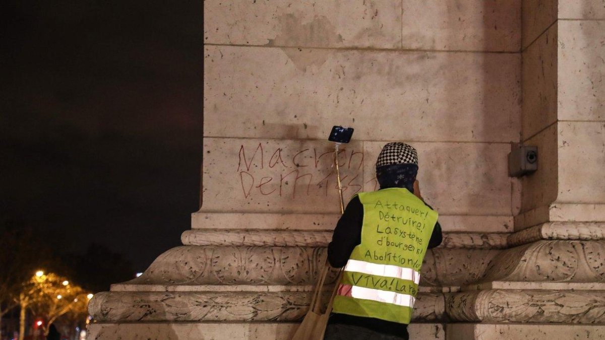 Anti-government protester scrawls graffiti that reads  Macron resign   on the wall of the Arc de Triumph in central Paris.