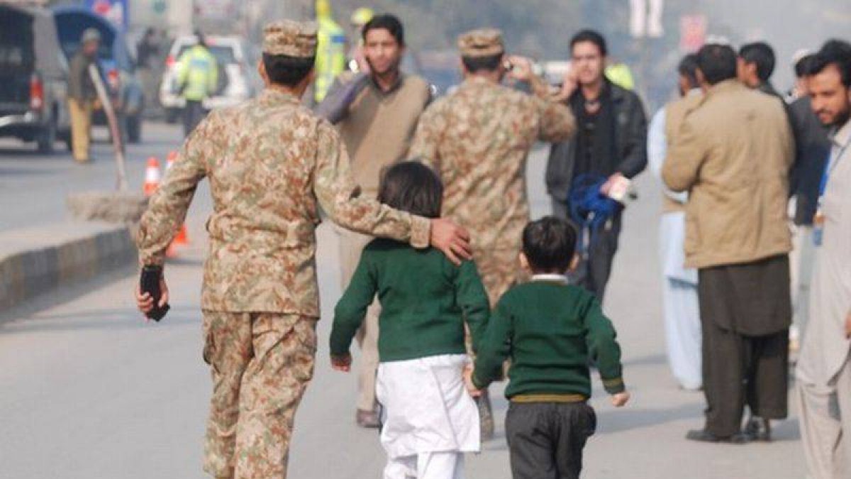 Un soldado paquistaní escolta a dos niños rescatados de la escuela que ha sufrido el ataque en Peshawar.
