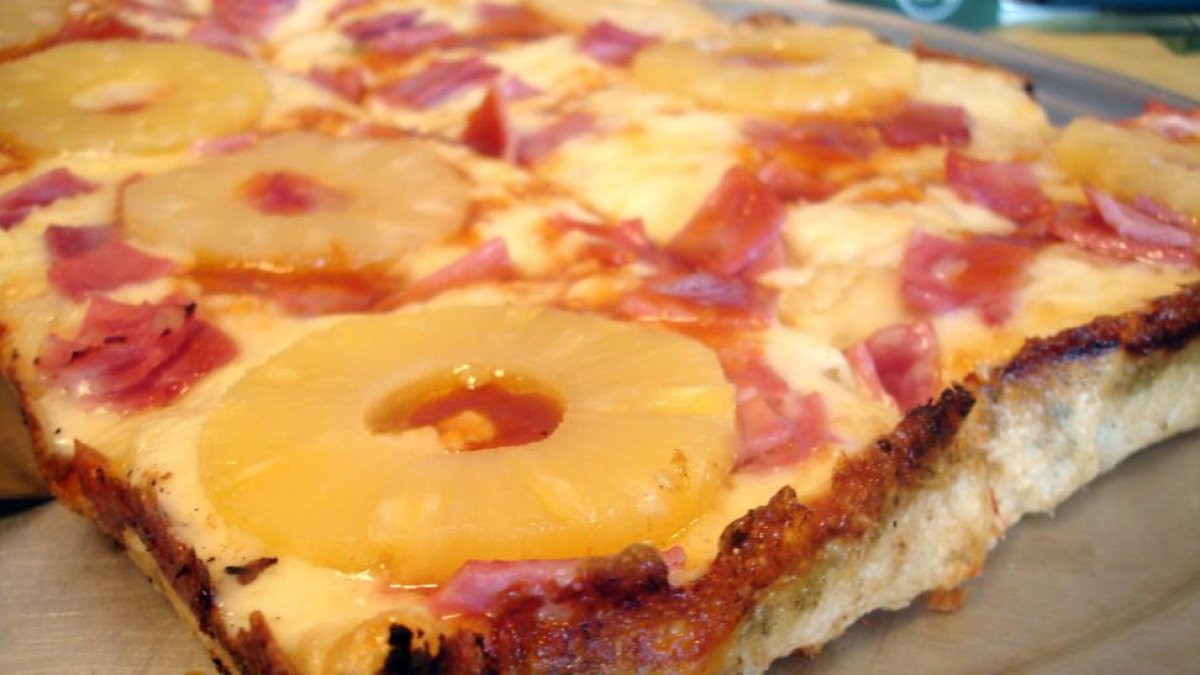 Una porción de pizza hawaiana, con rodajas de piña enteras.