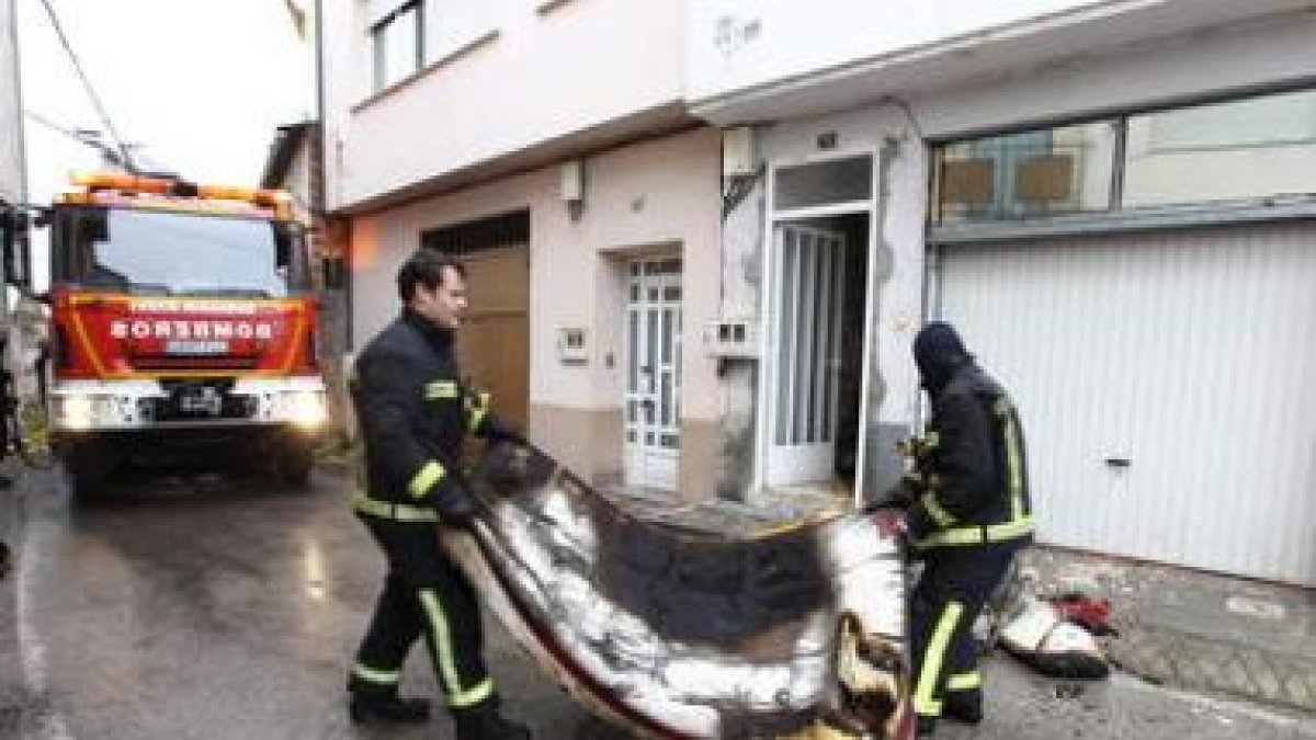 Dos bomberos sacan del interior de la casa uno de los colchones calcinados.