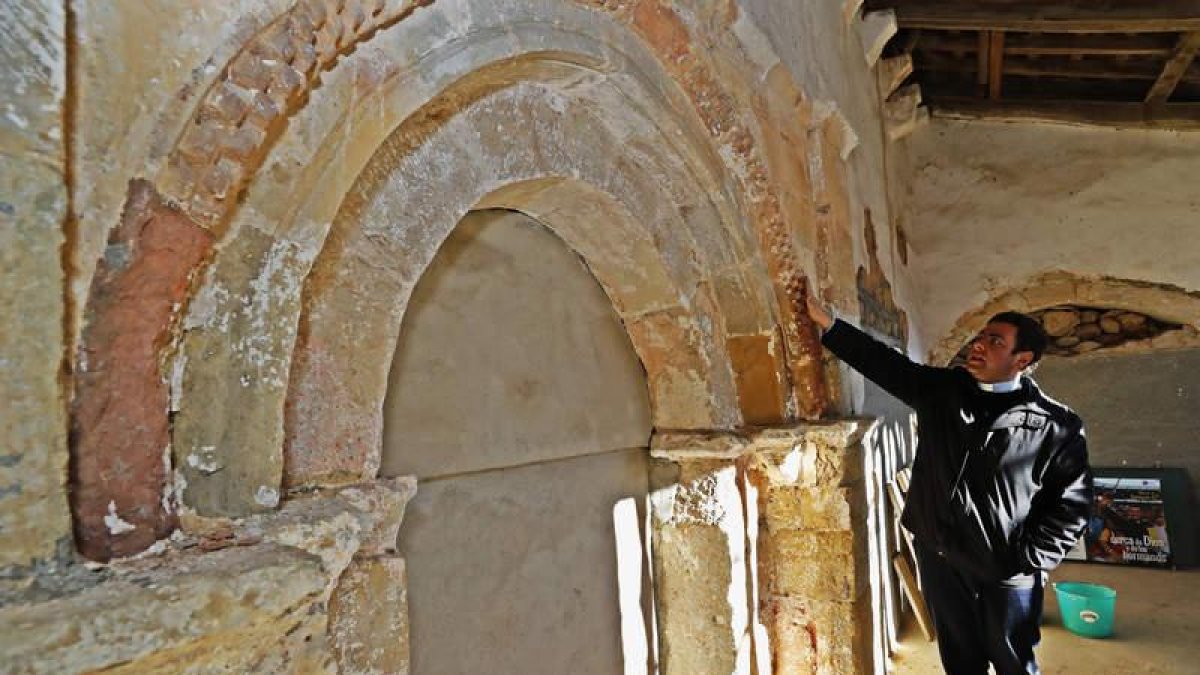 El párroco de San Pedro de Foncollada, Rubén Lorca, ante la portada románica ahora descubierta tras unas obras vecinales de mejora y saneamiento.