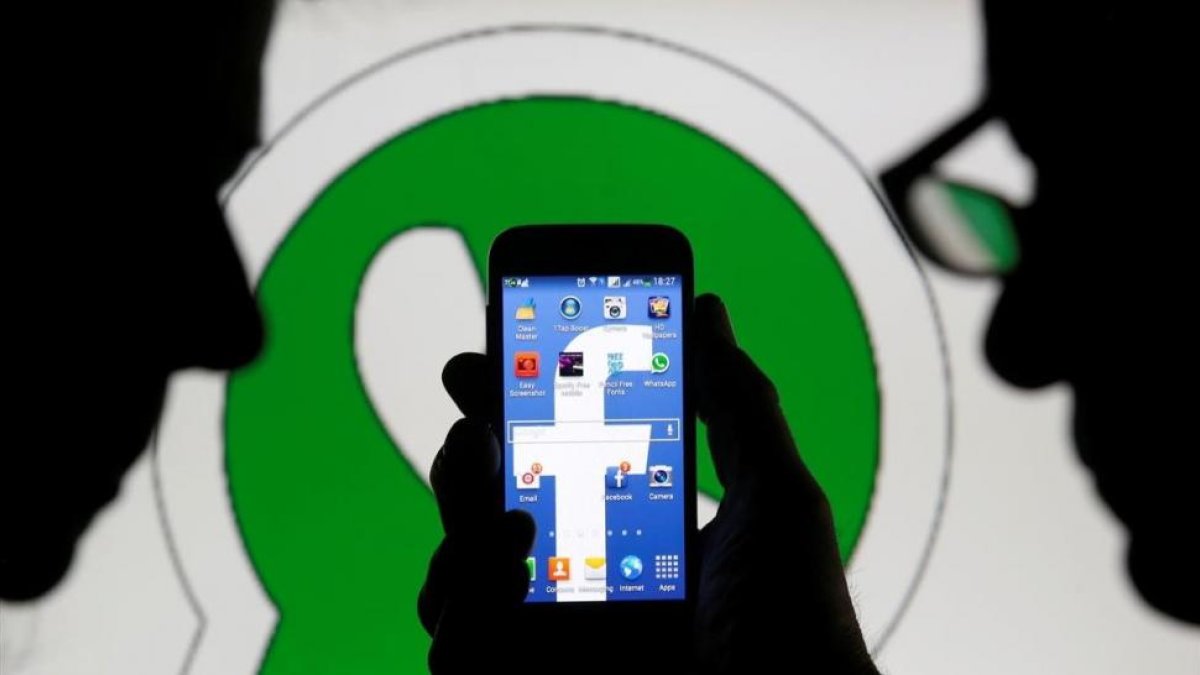 Dos hombres observan un smartphone con el logo de Facebook delante de una imagen del logo de Whatsapp.