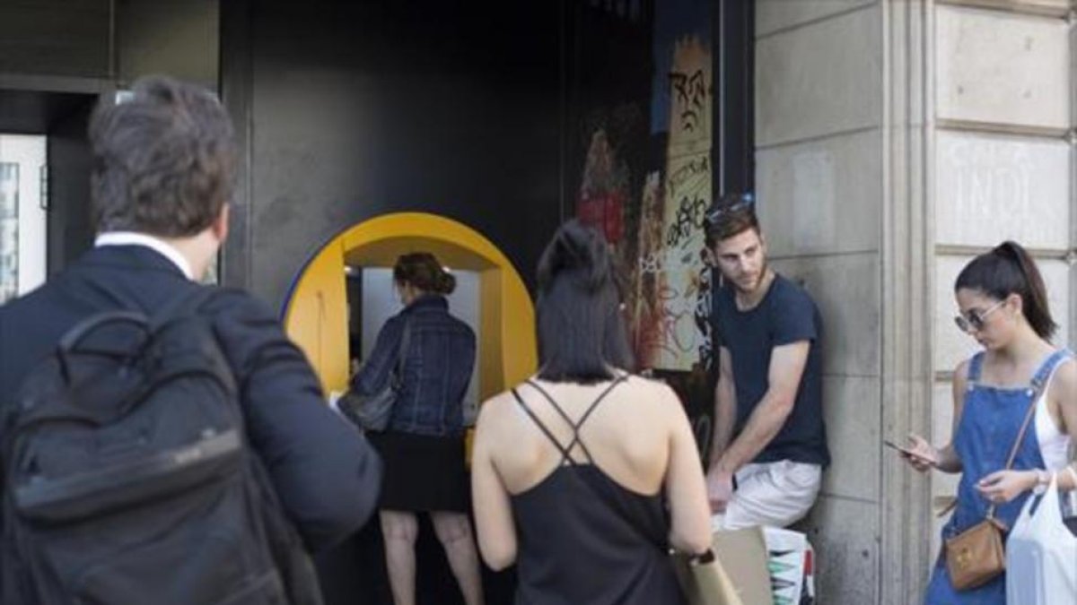 Varias personas esperan para operar en un cajero de una oficina de CaixaBank en la plaza de Catalunya.