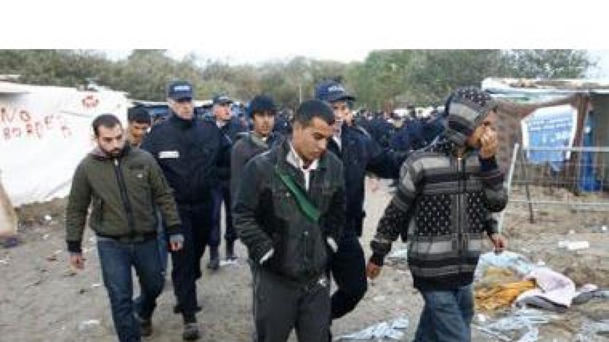 Varios policías detienen a un grupo de inmigrantes en un campamento, en Francia.