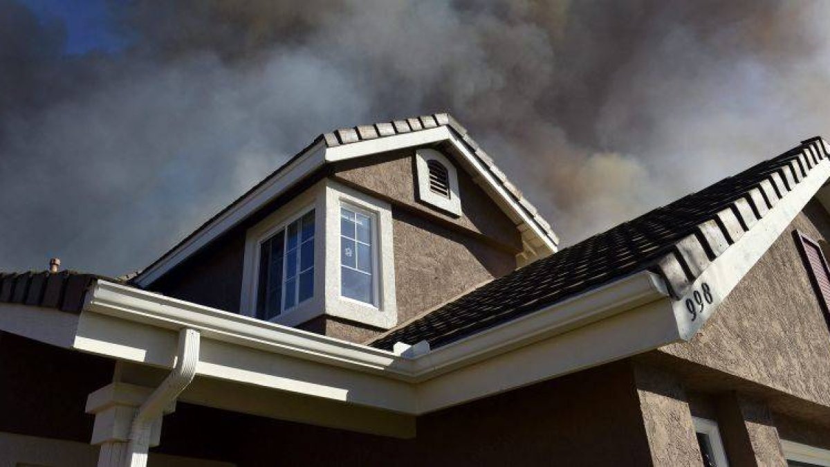 Una columna de humo emerge tras una casa en San Marcos, condado de San Diego (California).