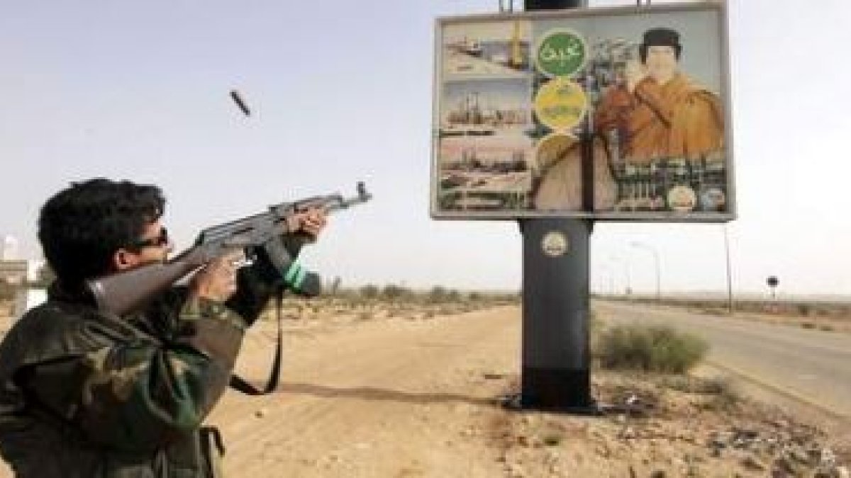 Un rebelde libio dispara contra una valla publicitaria con la imagen del coronel Muamar El Gadafi.
