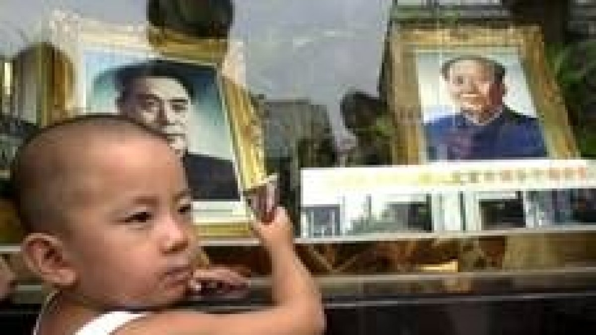 Un niño come un helado delante de los retratos de Zou Enlai y Mao