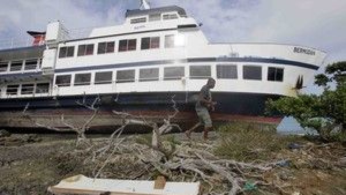Un hombre camina junto a un barco arrastrado hacia tierra por la fuerza del huracán Igor en Bermuda.