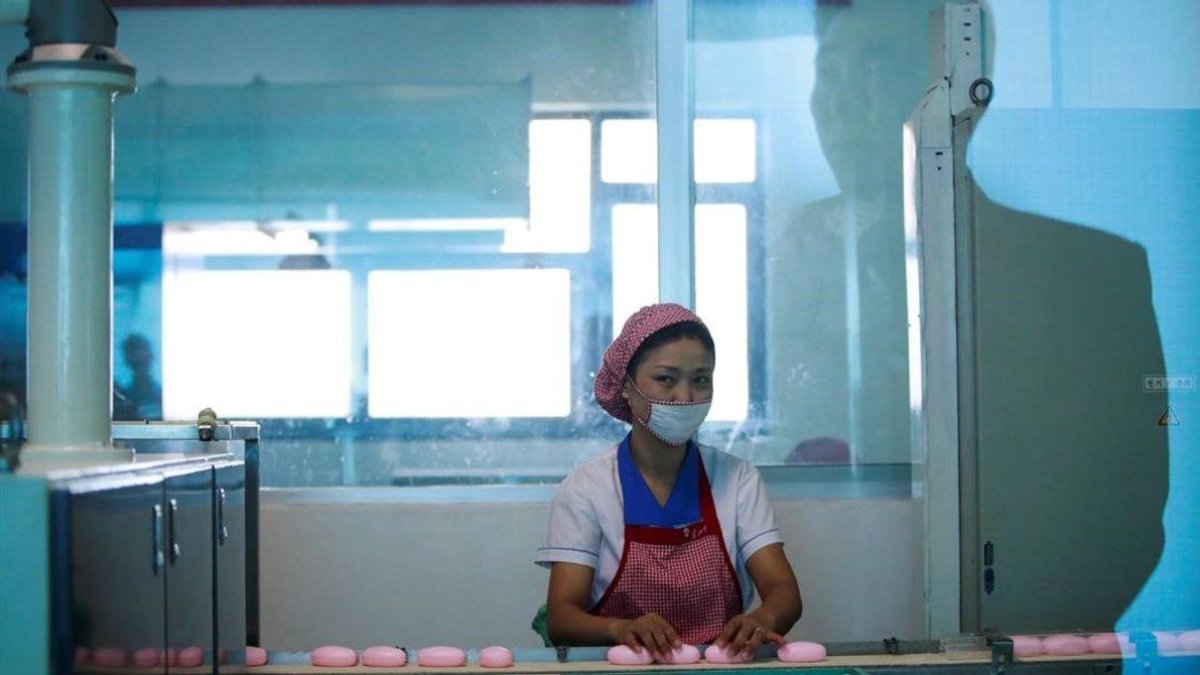 La silueta de un hombre aparece reflejada en el cristal mientras una empleada norcoreana trabaja en la cadena de produccion de jabones de la Fabrica de Cosmética de Pionyang, el 8 de septiembre del 2018.
