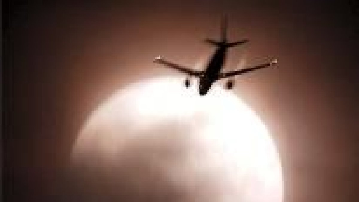 En la fotografía, un avión pasa junto a la luna eclipsada