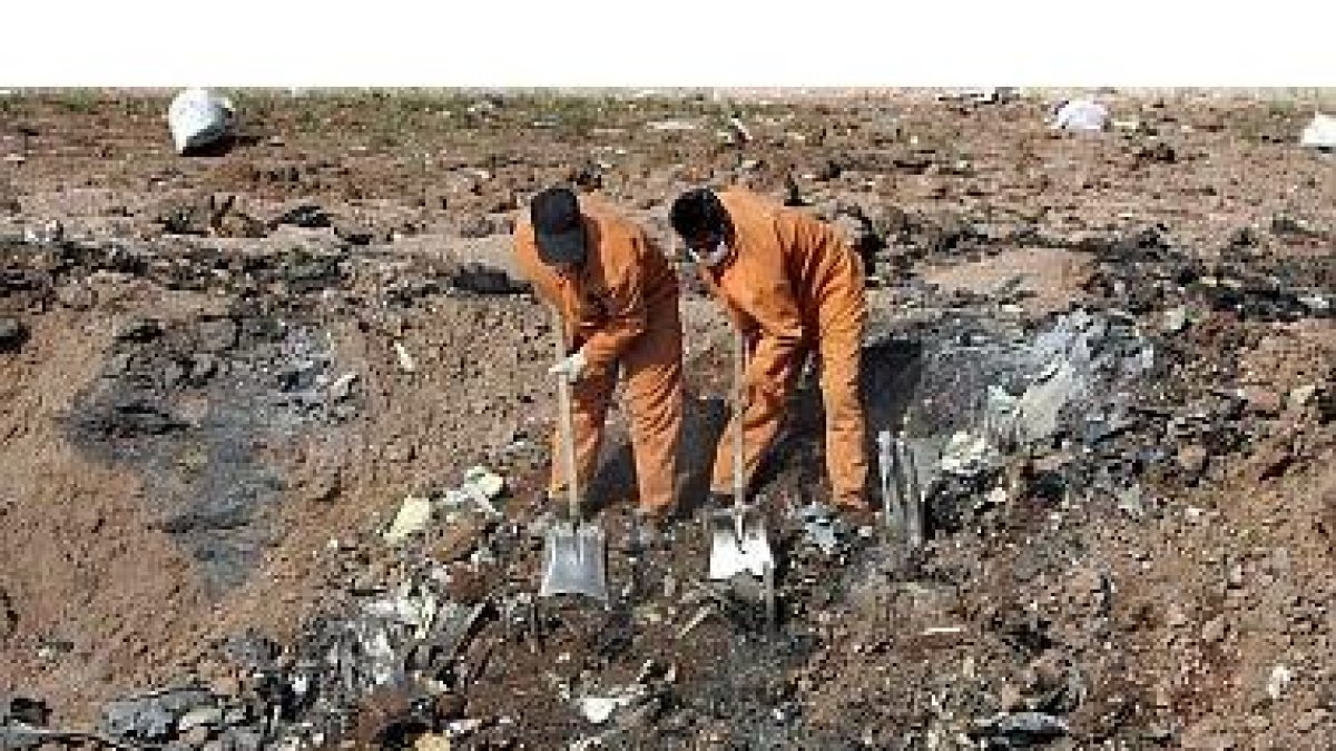 Dos operarios trabajan limpian los escombros del avión.