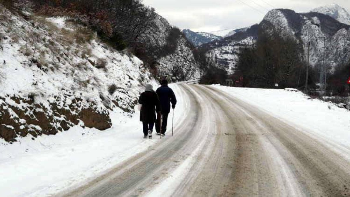 Dos ancianos caminan por una carretera nevada cerca de un pueblo de la  montaña leonesa.