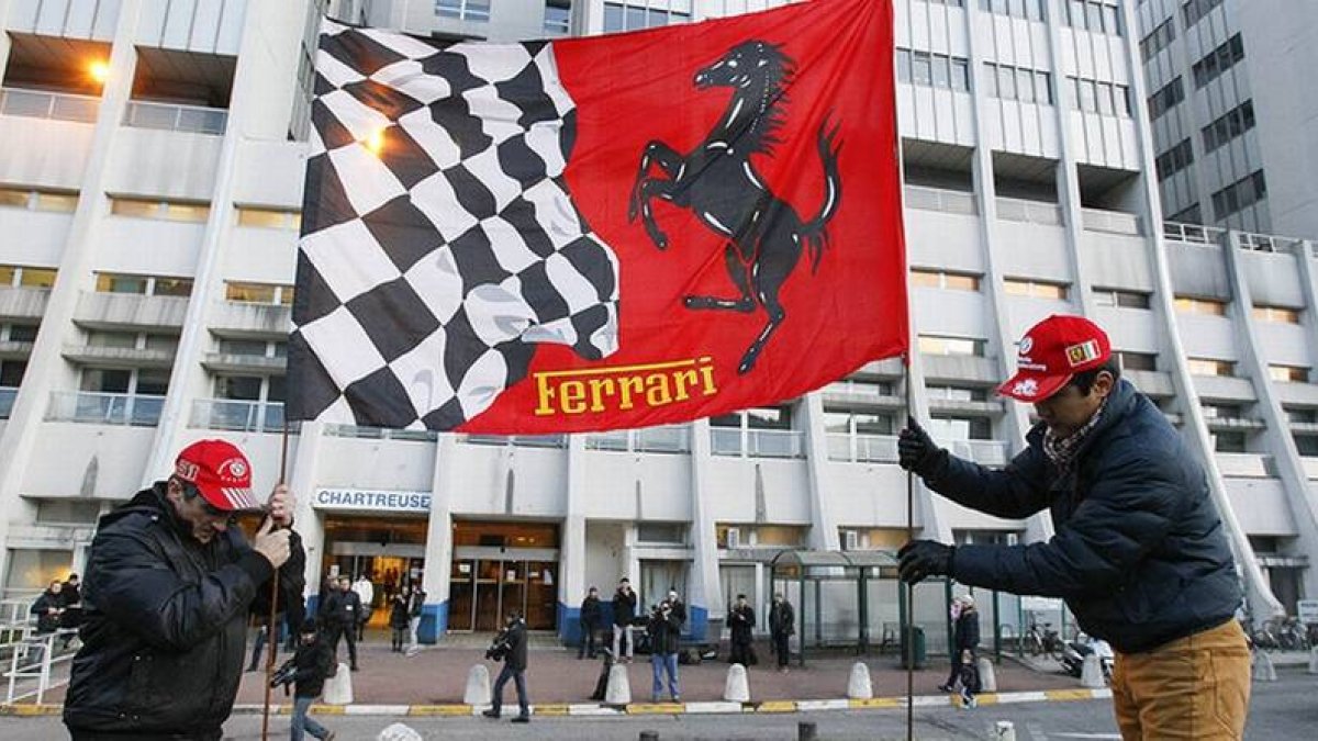 Dos aficionados de Ferrari colocan una bandera de la escuadería ante el hospital de Grenoble donde está ingresado Schumacher.