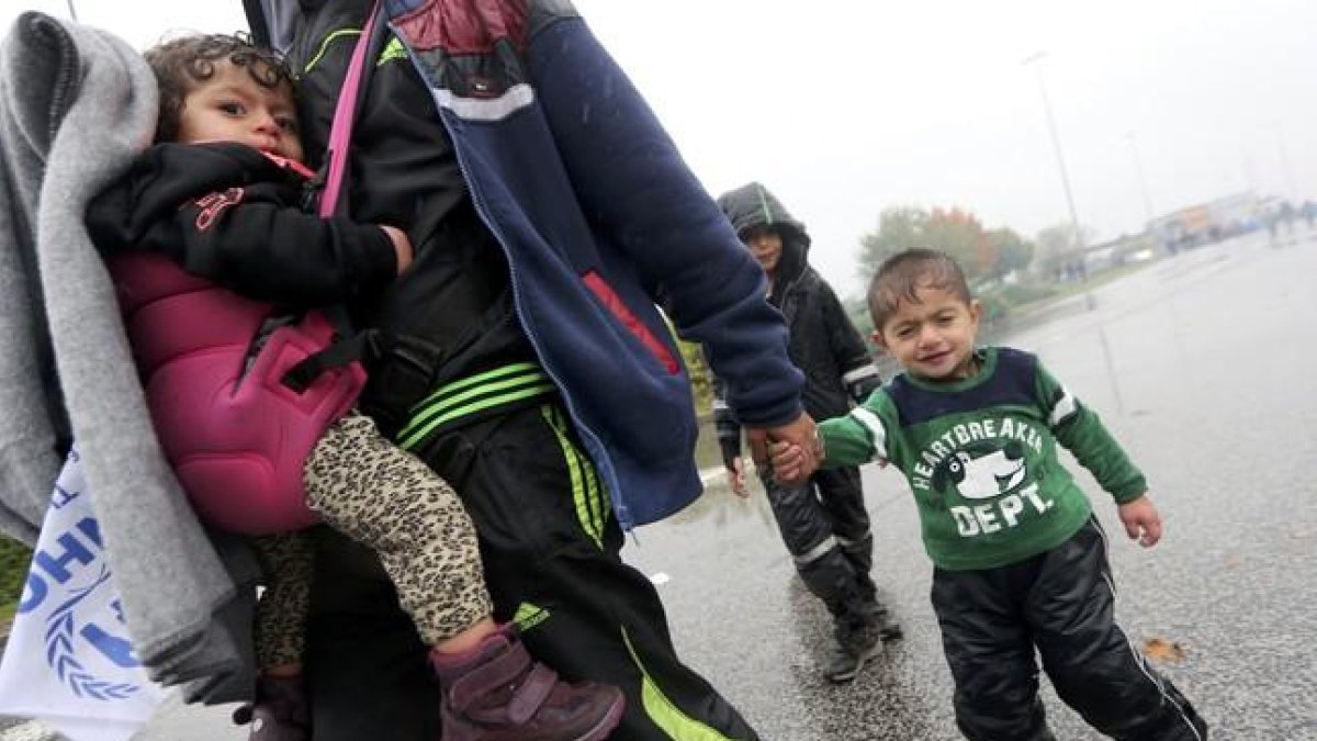 Un hombre camina llevando a dos niños bajo la lluvia junto a la frontera con Eslovenia.
